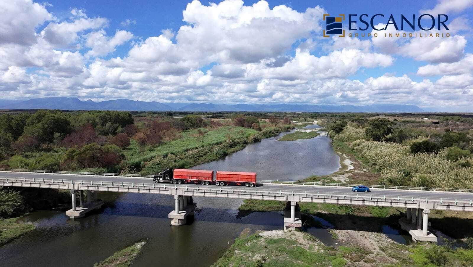 Tráiler cruzando un puente de autopista sobre el río, con la sierra al fondo